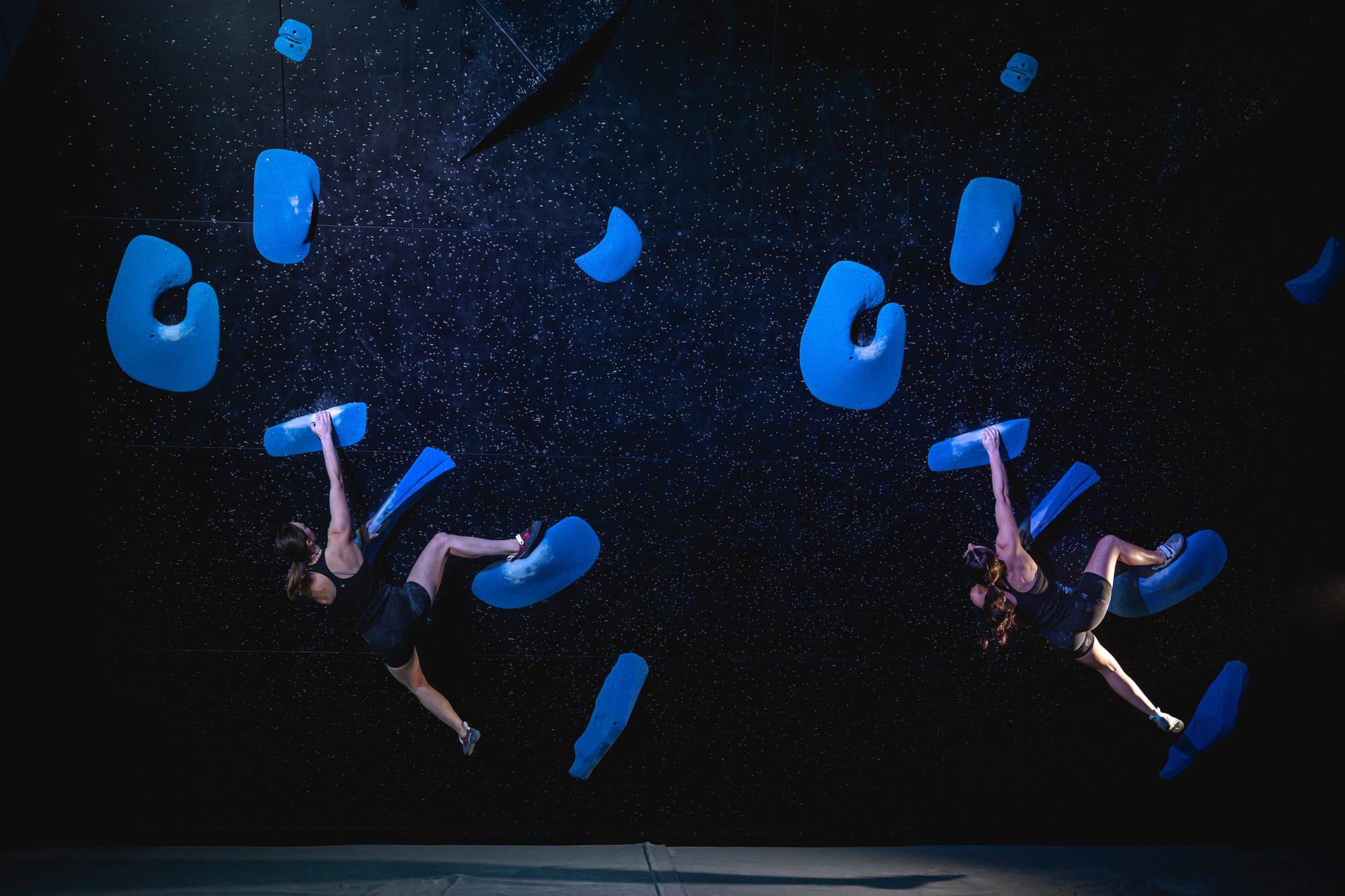 Two climbers climbing next to each other on identical boulders
